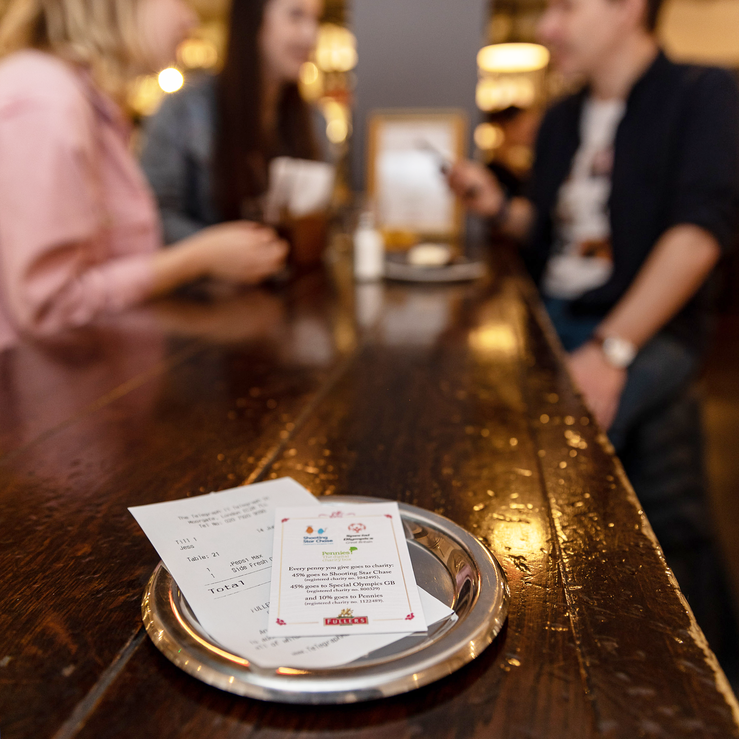 Customers in a Fuller's pub enjoy drinks, with details on the Pennies micro-donation opportunity presented to them with their bill