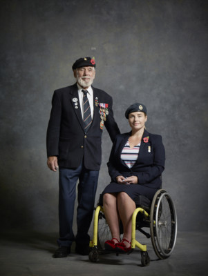 Two Royal British Legion veterans, a woman using a wheelchair, and man standing beside her. Their morning suits carry their medals, and both wear poppies.