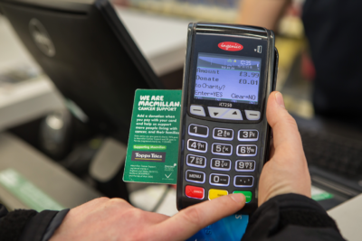 A customer makes a donation in-store at Topps Tiles. The point of sale card attachment clearly displays the nominated charity, Macmillan Cancer Support.